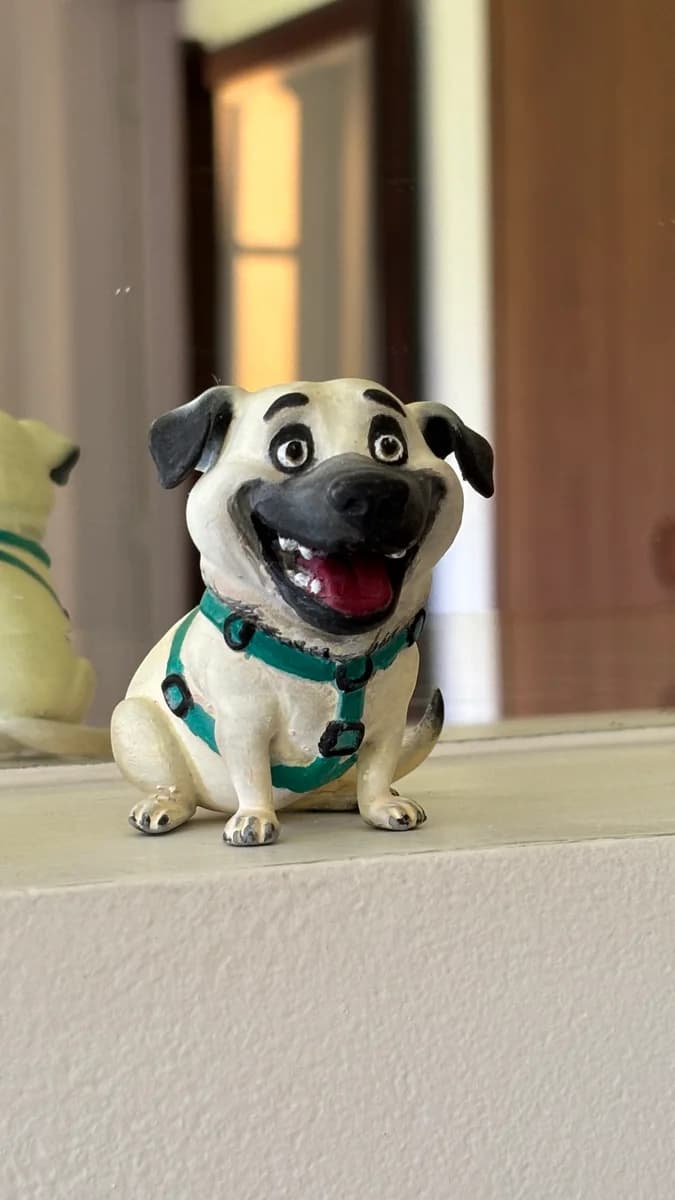 Close da miniatura do Bethoven, cachorro bege de peitoral azul-petróleo, sentado e sorrindo com a língua de fora