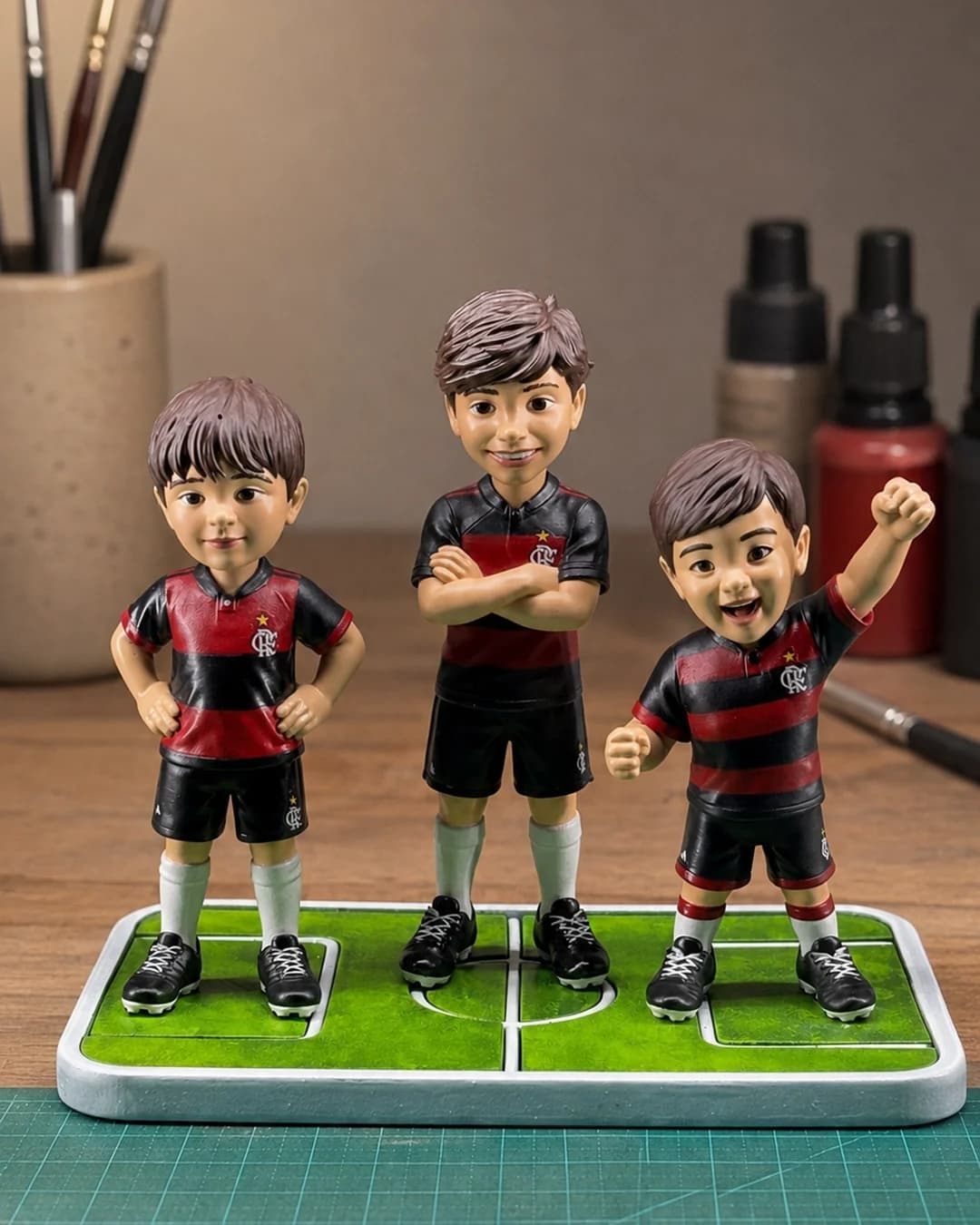 As três miniaturas personalizadas dos primos torcedores, com o manto rubro-negro do Flamengo, sobre uma base em forma de campo de futebol