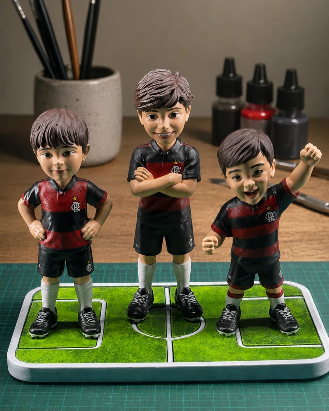 As três miniaturas de time ao lado dos vidros de tinta e dos pincéis usados na pintura à mão